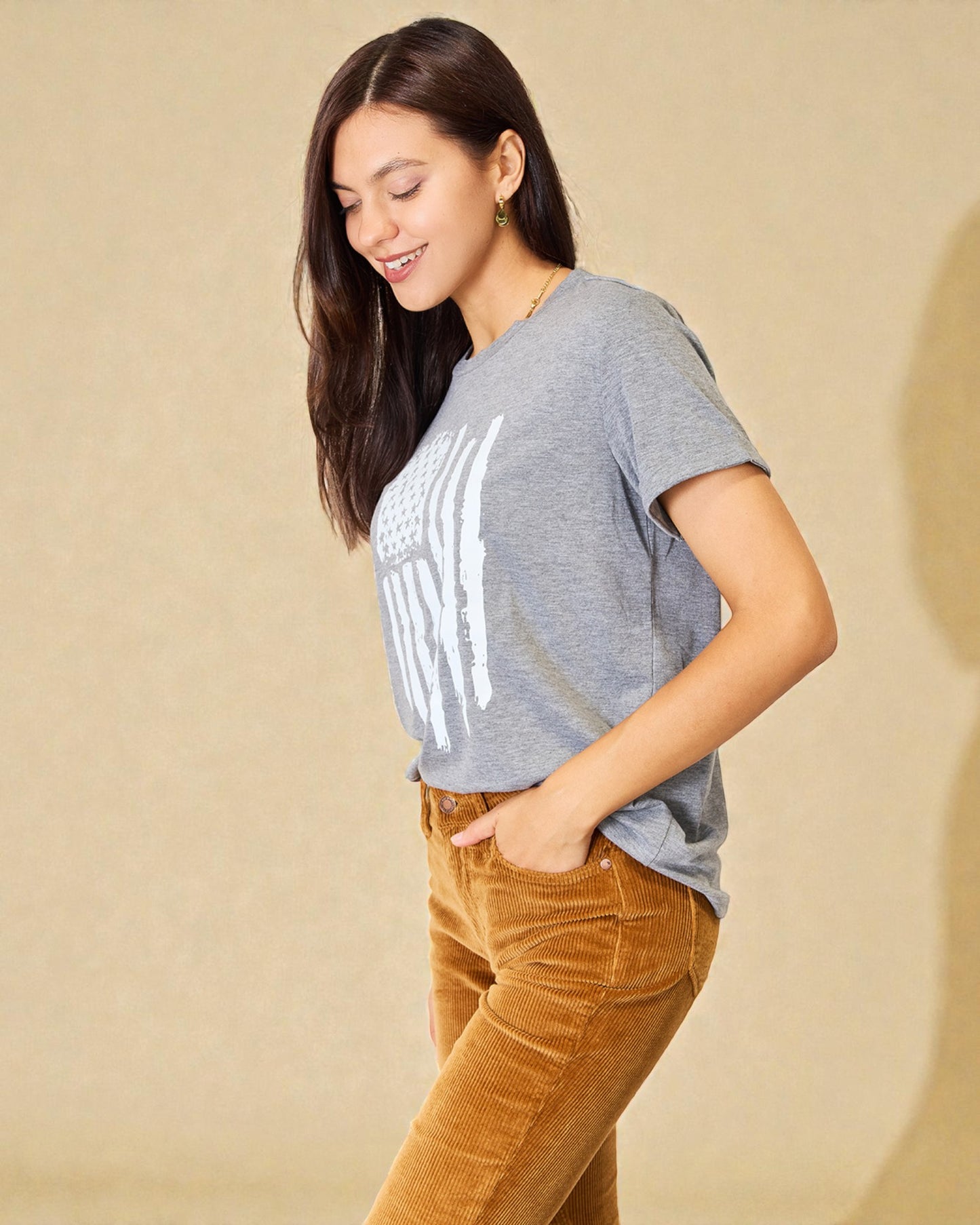 Woman wearing a gray t-shirt with text and brown pants against a beige background