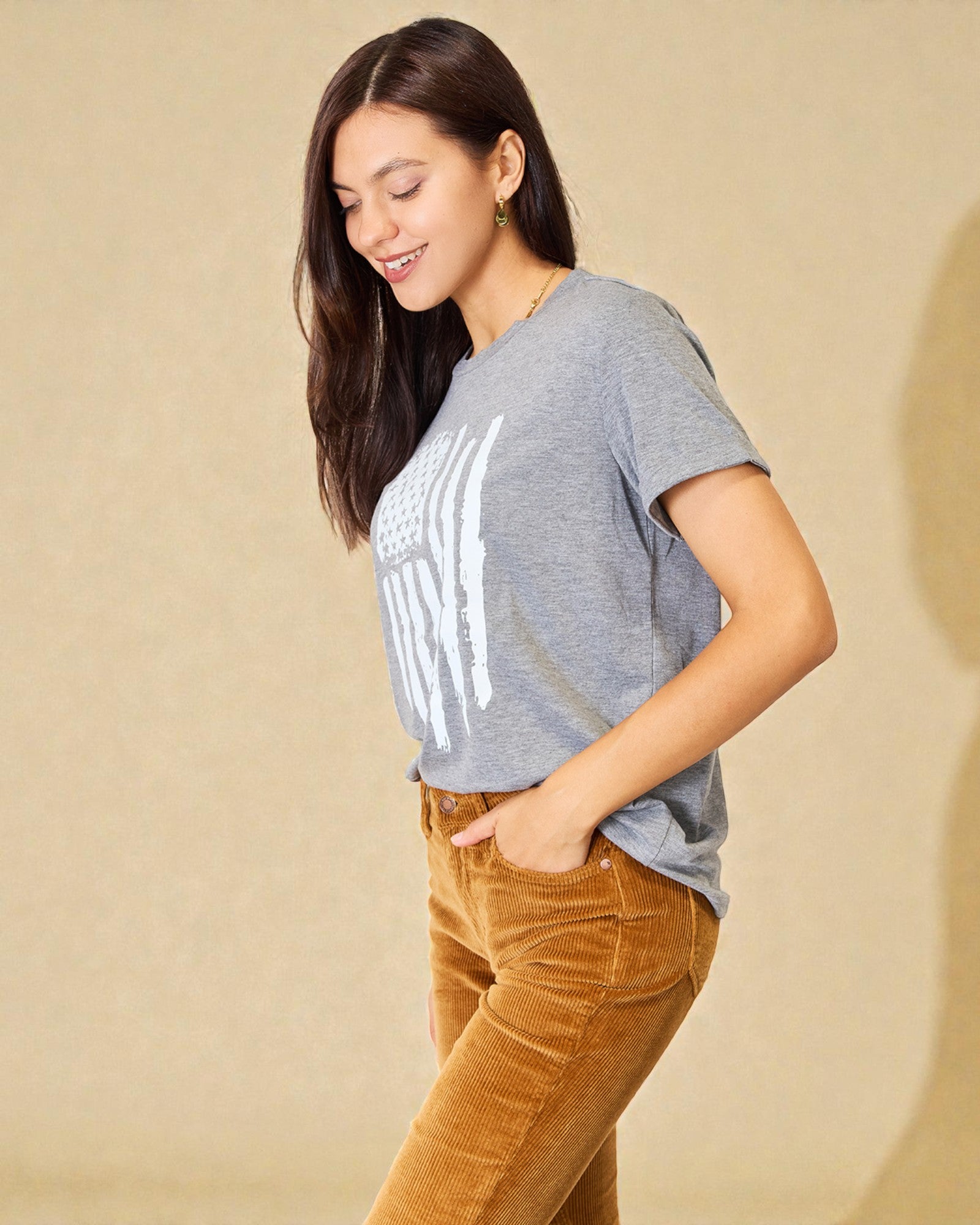 Woman wearing a gray t-shirt with text and brown pants against a beige background