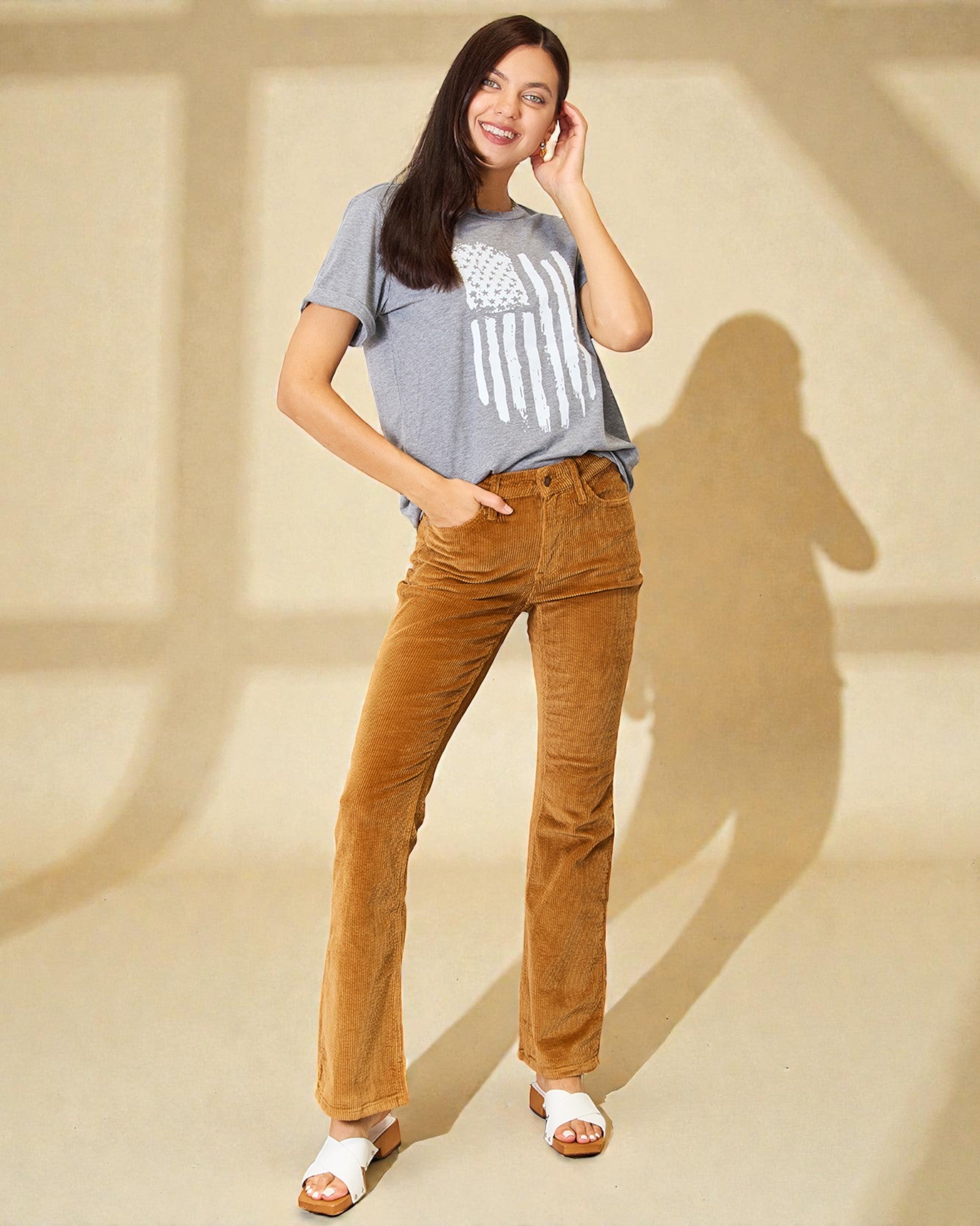 Woman wearing a gray t-shirt with a graphic design and brown pants on a beige background