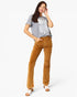 A woman modeling a gray t-shirt with a white distressed American flag graphic and brown corduroy flare pants, standing against a light gray studio background.