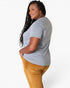A woman wearing a heather gray short-sleeve t-shirt and mustard yellow corduroy pants, shown from a side-back angle against a plain white studio background.
