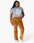A woman modeling a heather gray t-shirt with a white distressed American flag graphic and brown corduroy pants, standing against a light gray studio background.