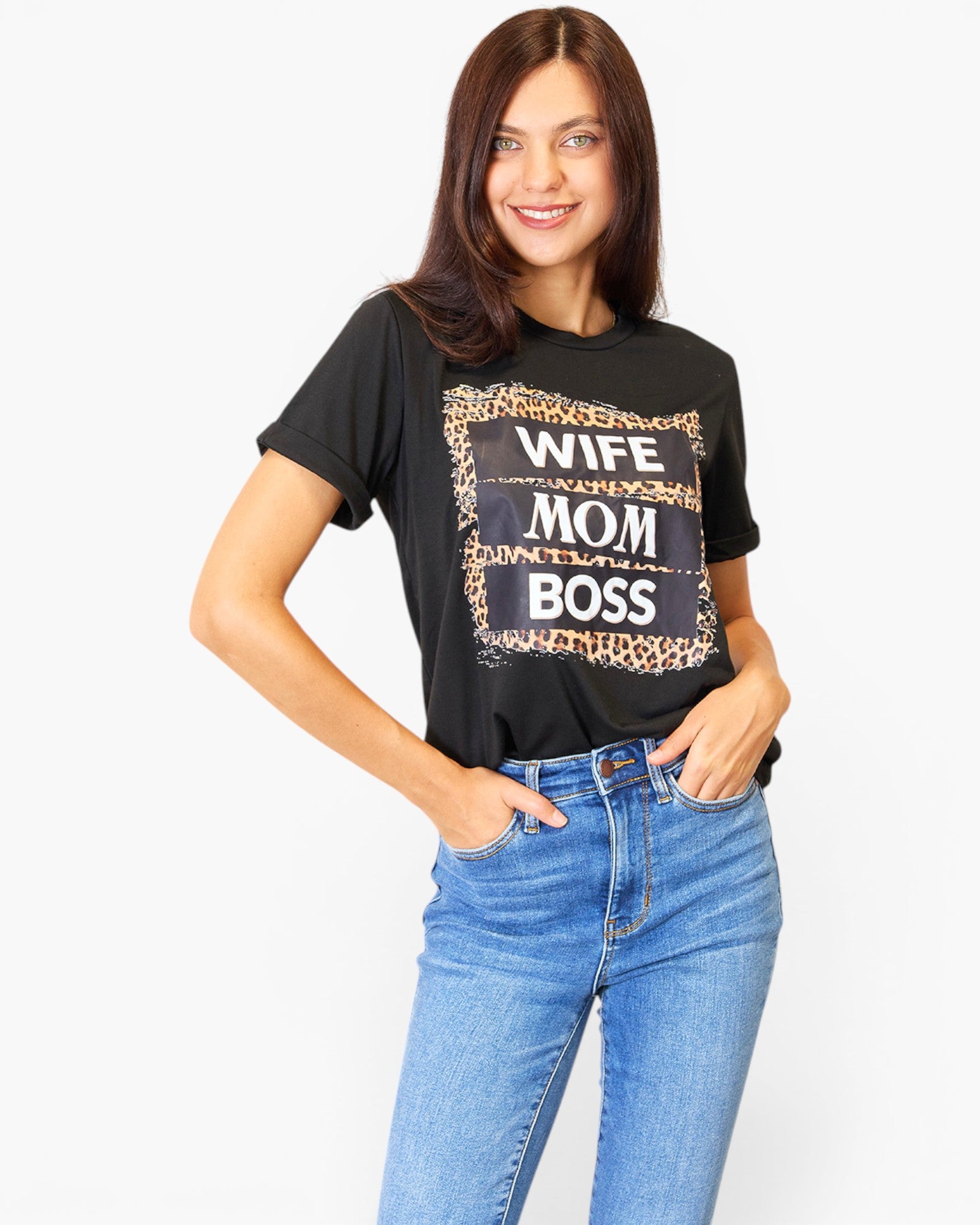 A woman modeling a black graphic t-shirt with a leopard print and white text reading 'WIFE MOM BOSS', paired with blue jeans, against a plain white background.