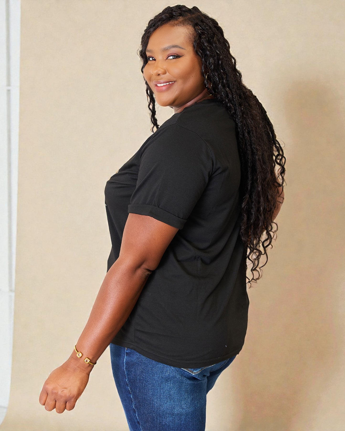 Woman wearing a black t-shirt and blue jeans against a beige background