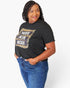 A woman wearing a black graphic t-shirt with a leopard print and white text that reads 'WIFE MOM BOSS', paired with blue jeans, against a plain white background.