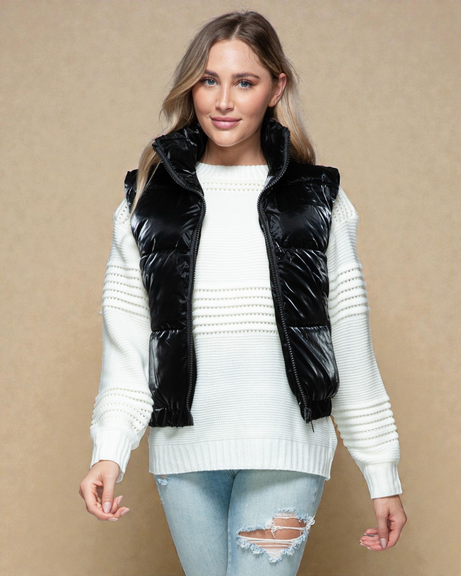 Woman wearing a black puffer vest over a white sweater on a beige background