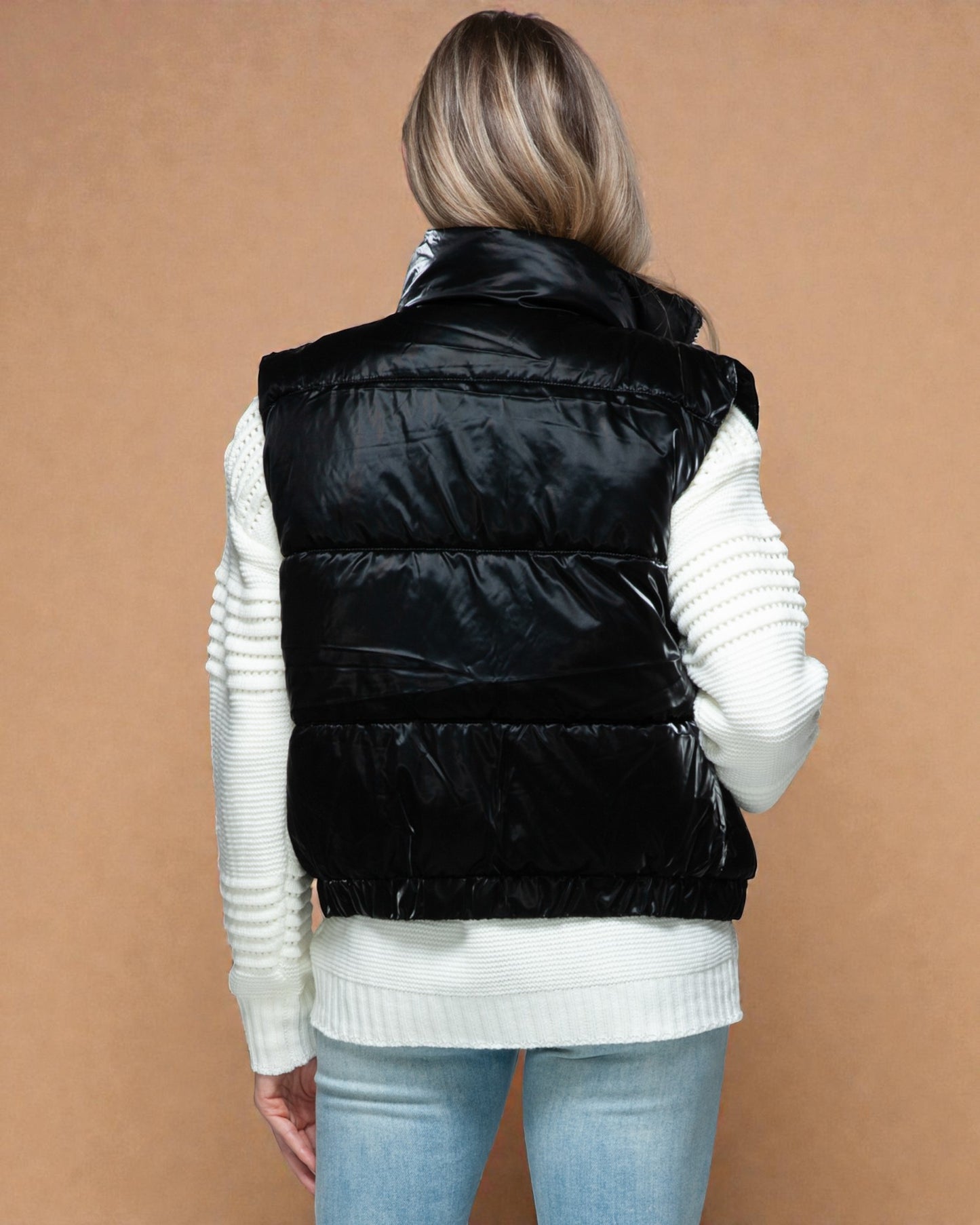 Person wearing a black puffer vest over a white sweater on a brown background