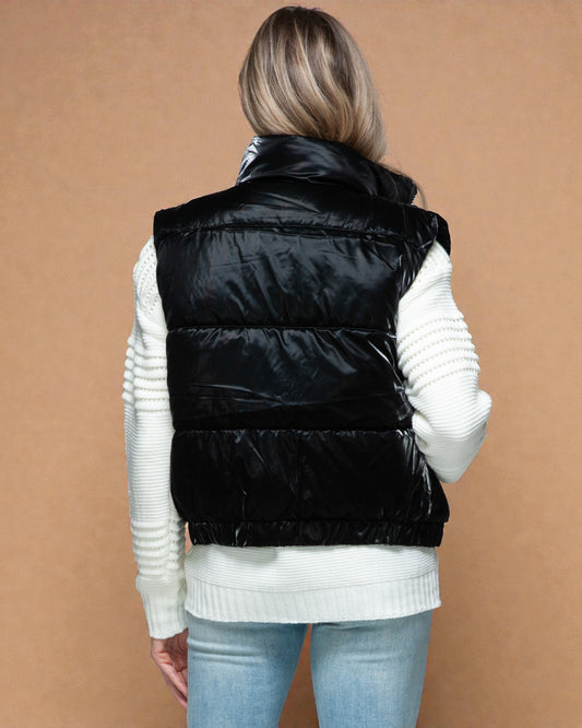 Person wearing a black puffer vest over a white sweater on a brown background