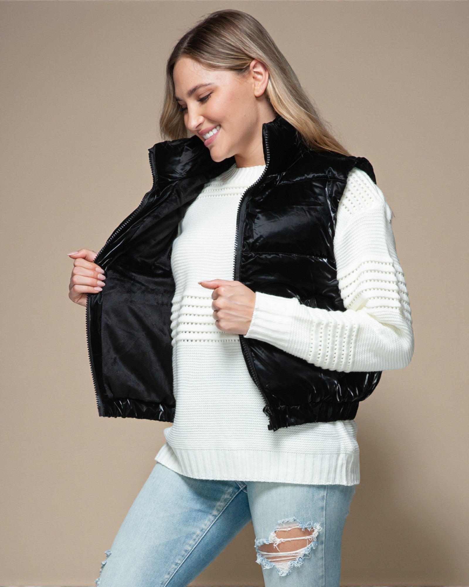 Woman wearing a black puffer vest over a white sweater on a beige background