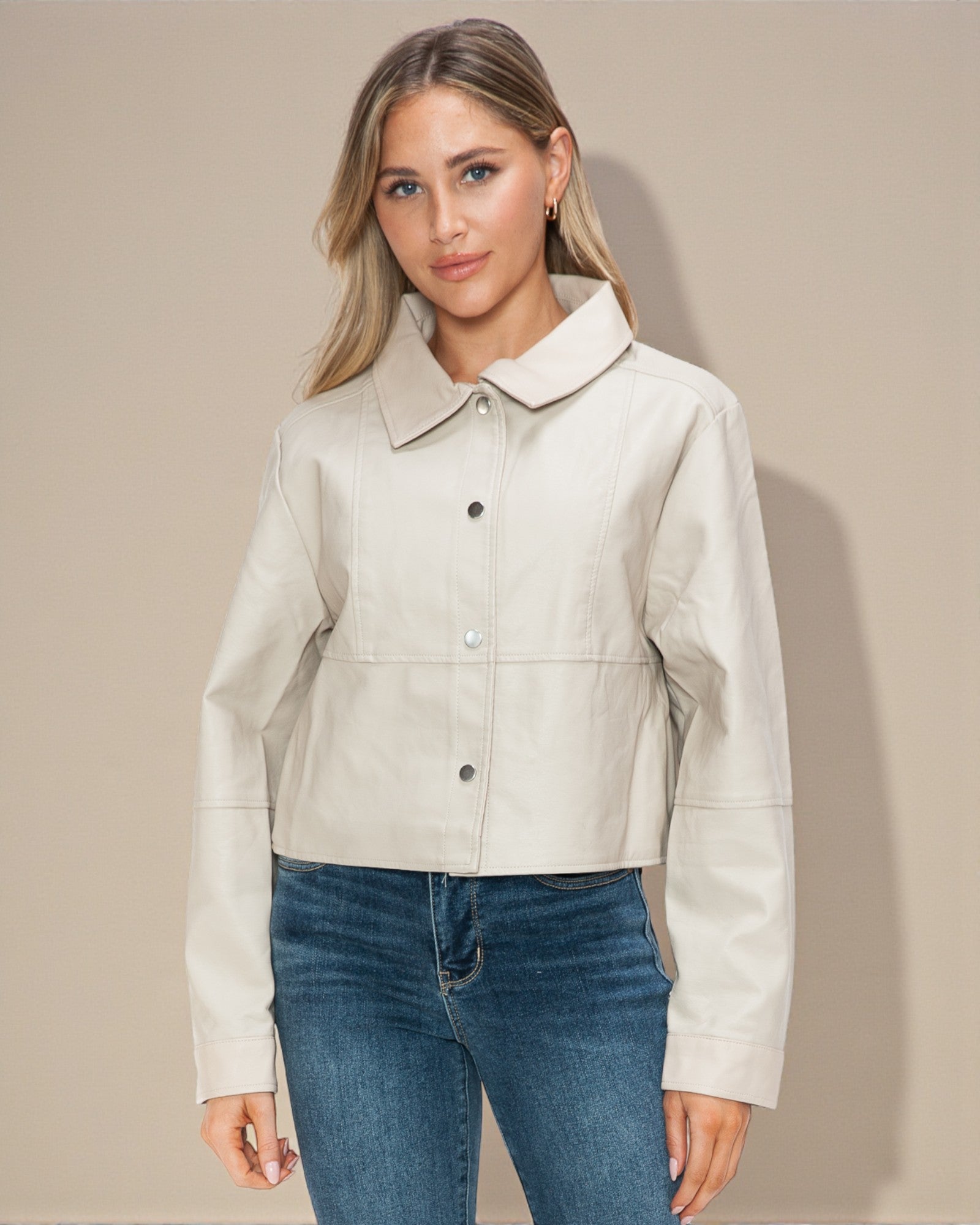 Woman wearing a beige jacket and blue jeans against a beige background