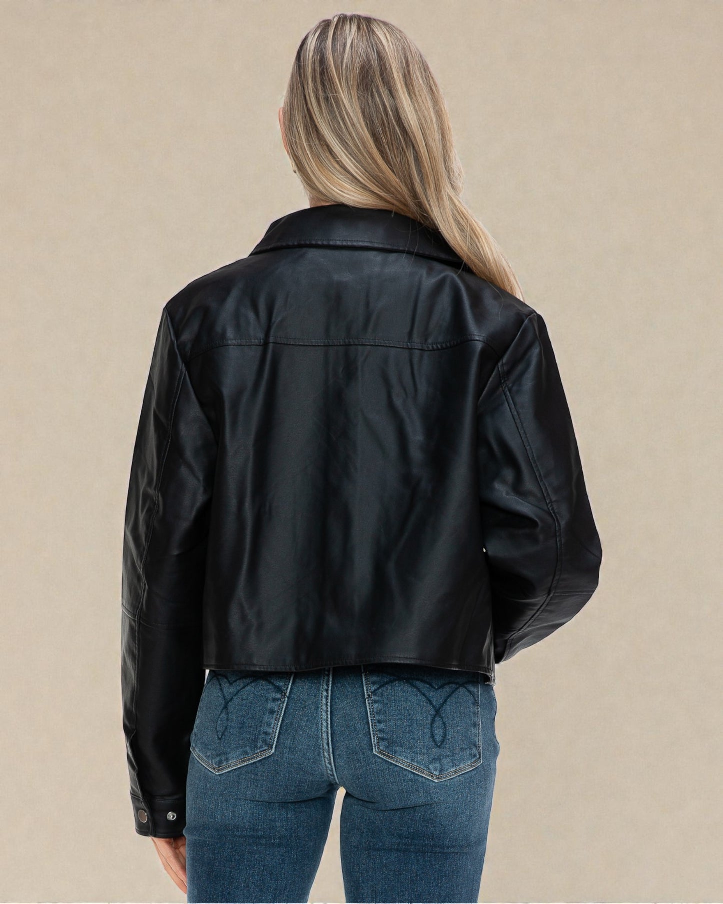 Person wearing a black leather jacket and blue jeans on a beige background