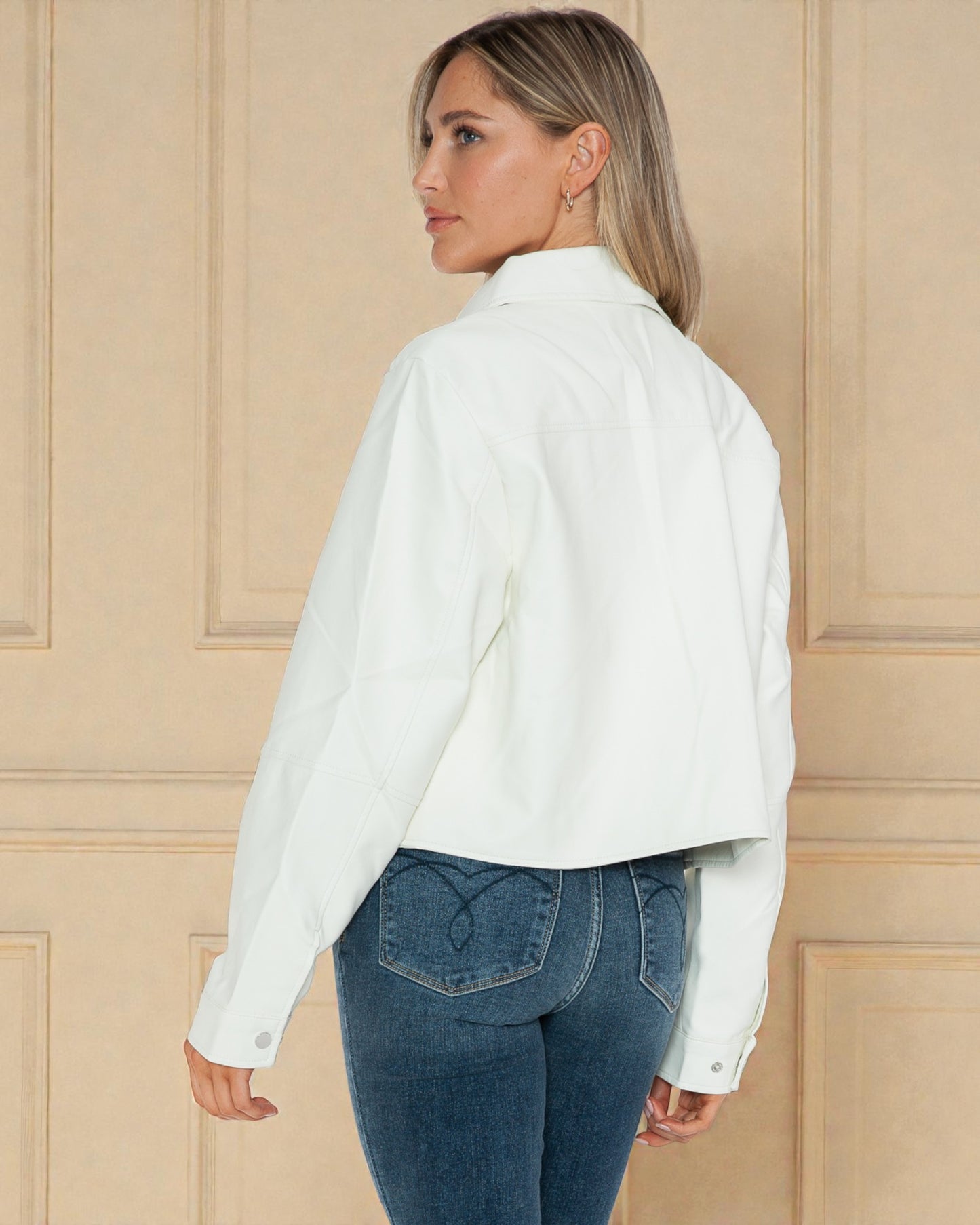 Woman wearing a white shirt and blue jeans against a beige paneled wall.