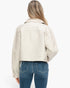 A woman viewed from the back wearing a cropped off-white leather jacket and blue jeans against a plain white background.