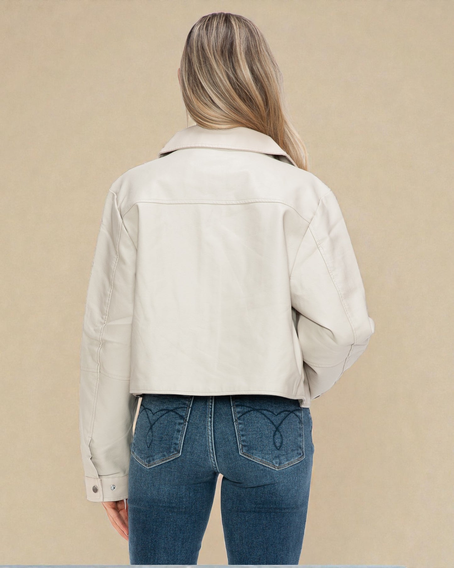Person wearing a beige jacket and blue jeans on a beige background