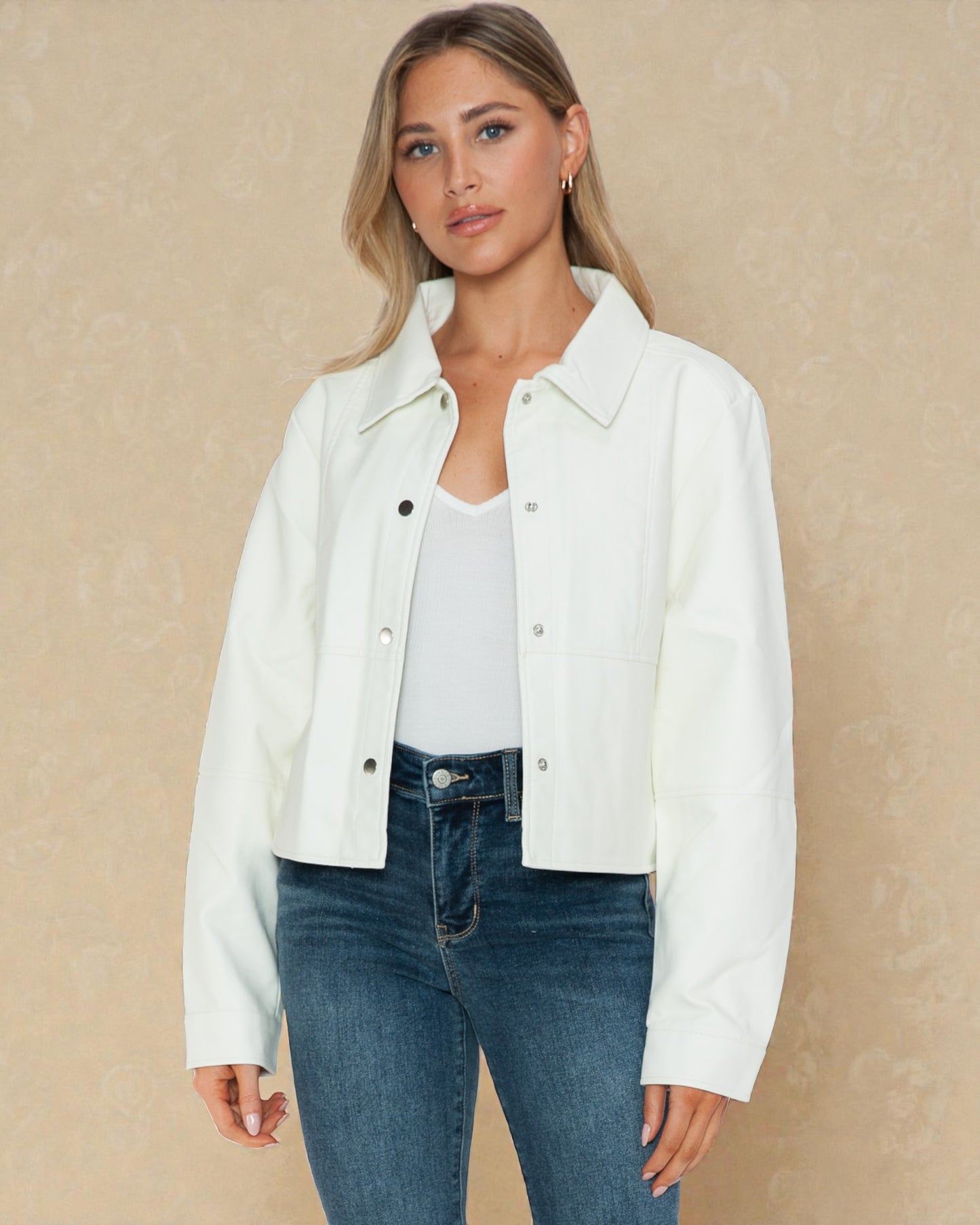 Woman wearing a white jacket over a white shirt and blue jeans on a beige background