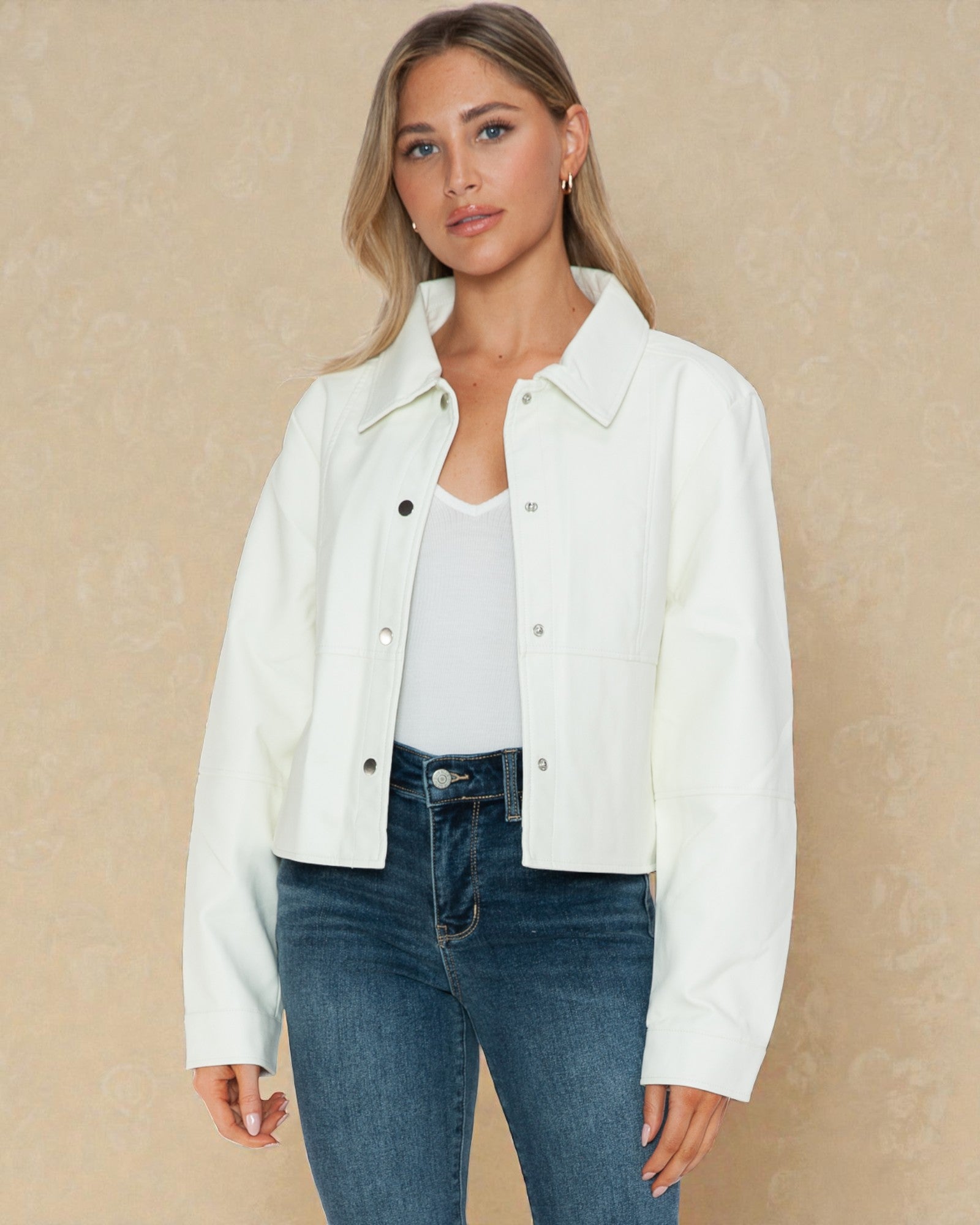 Woman wearing a white jacket over a white shirt and blue jeans on a beige background