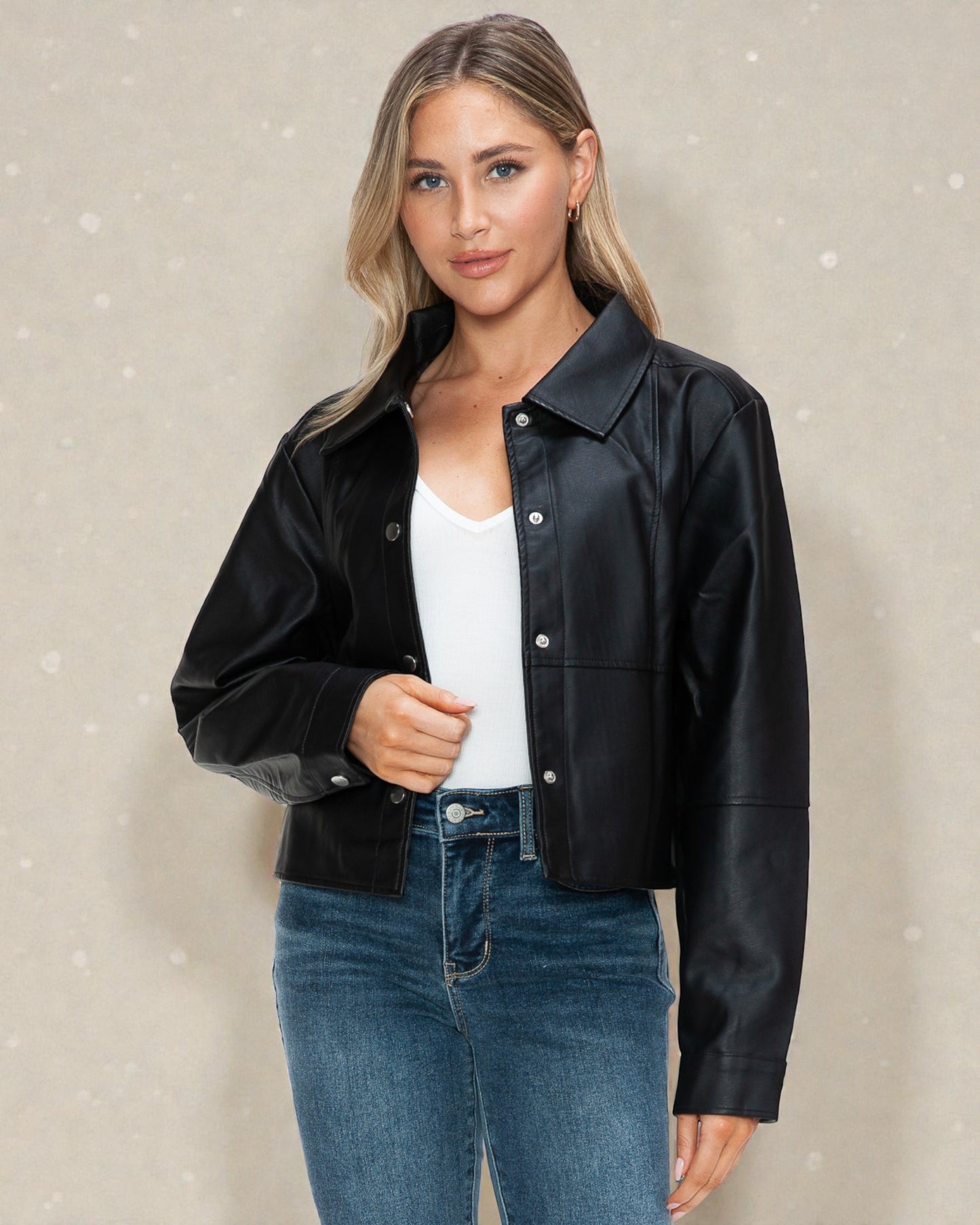 Woman wearing a black leather jacket over a white top and blue jeans on a beige background