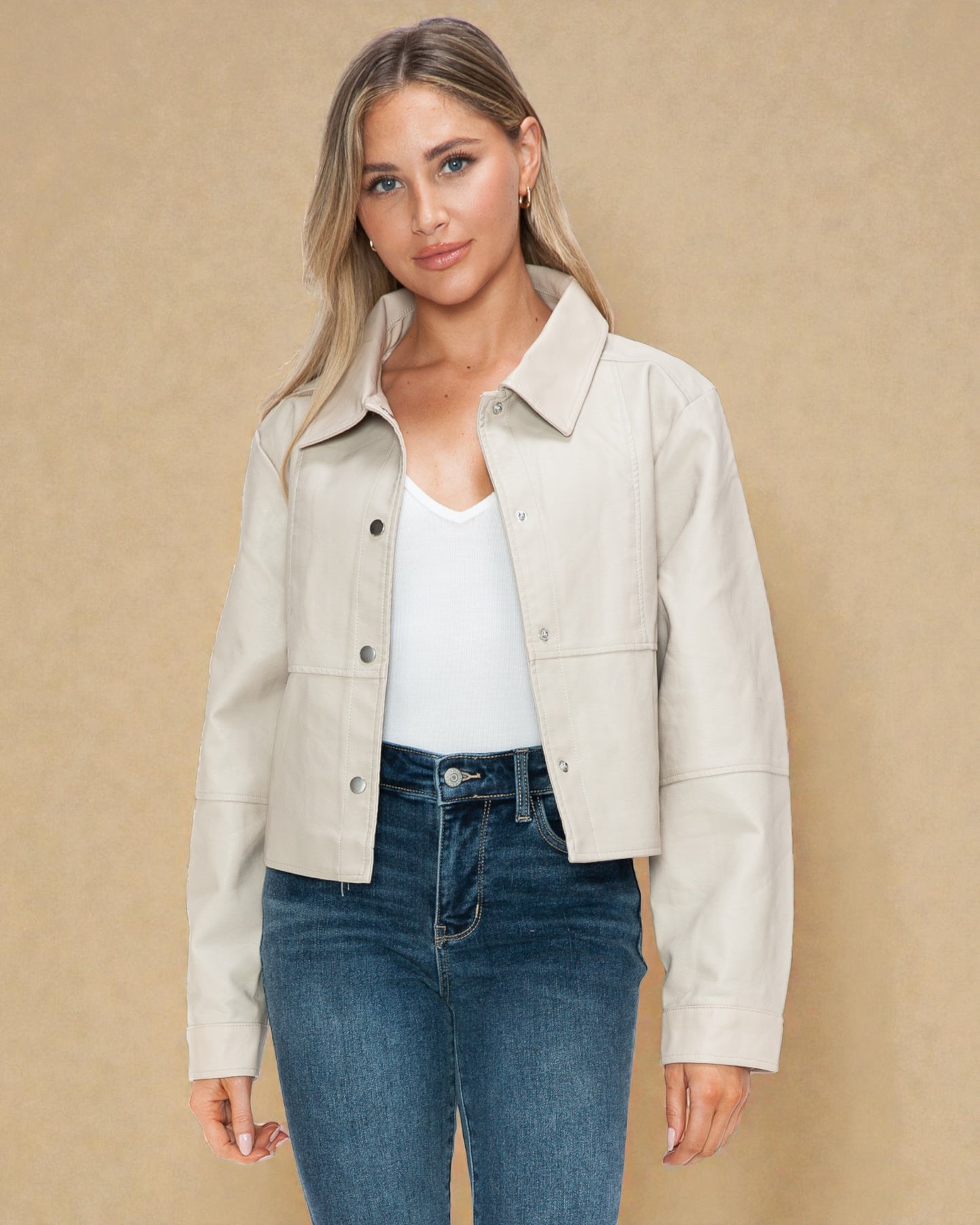 Woman wearing a beige jacket over a white top and blue jeans on a beige background
