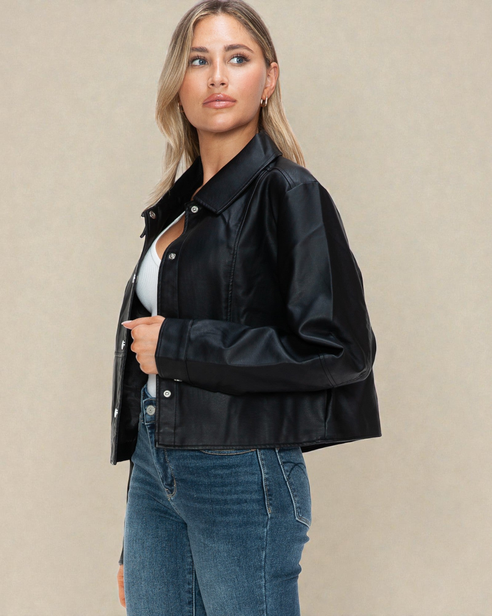 Woman wearing a black jacket and blue jeans against a beige background