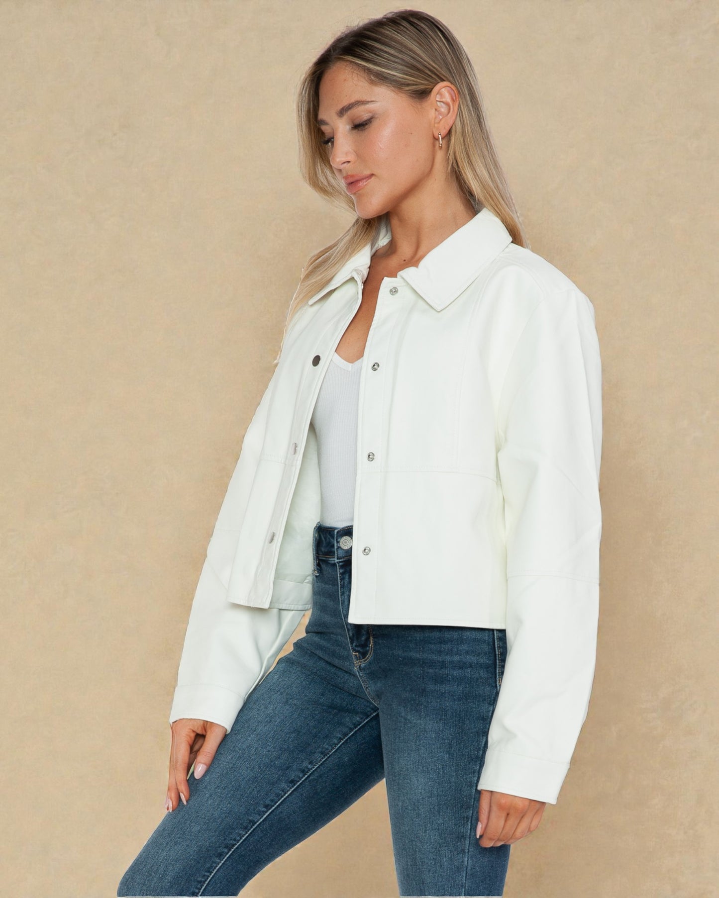 Woman wearing a white jacket and blue jeans against a beige background