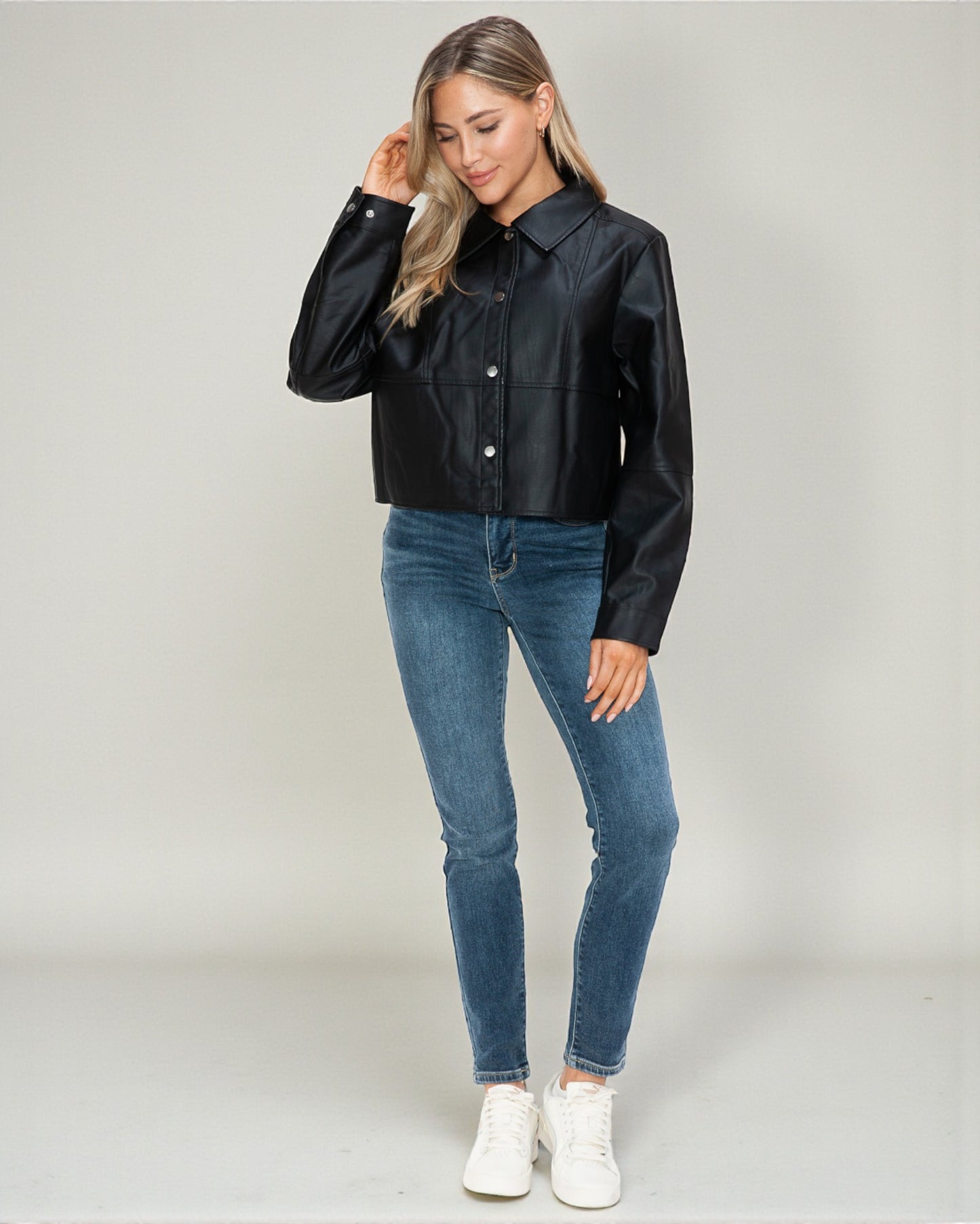 Woman wearing a black leather jacket and blue jeans on a plain background