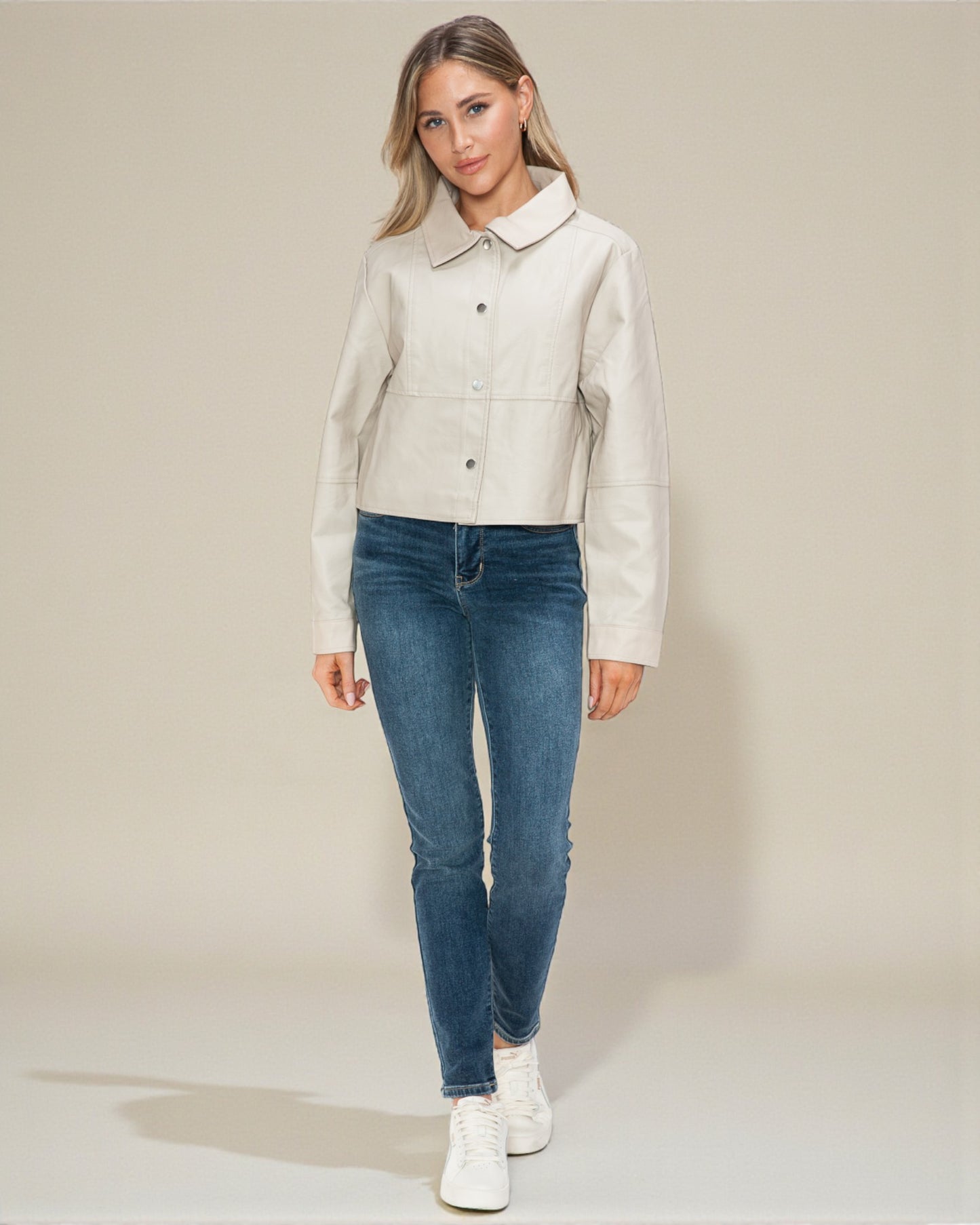 Woman wearing a light-colored jacket and blue jeans on a plain background