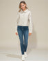 Woman wearing a light-colored jacket and blue jeans on a plain background