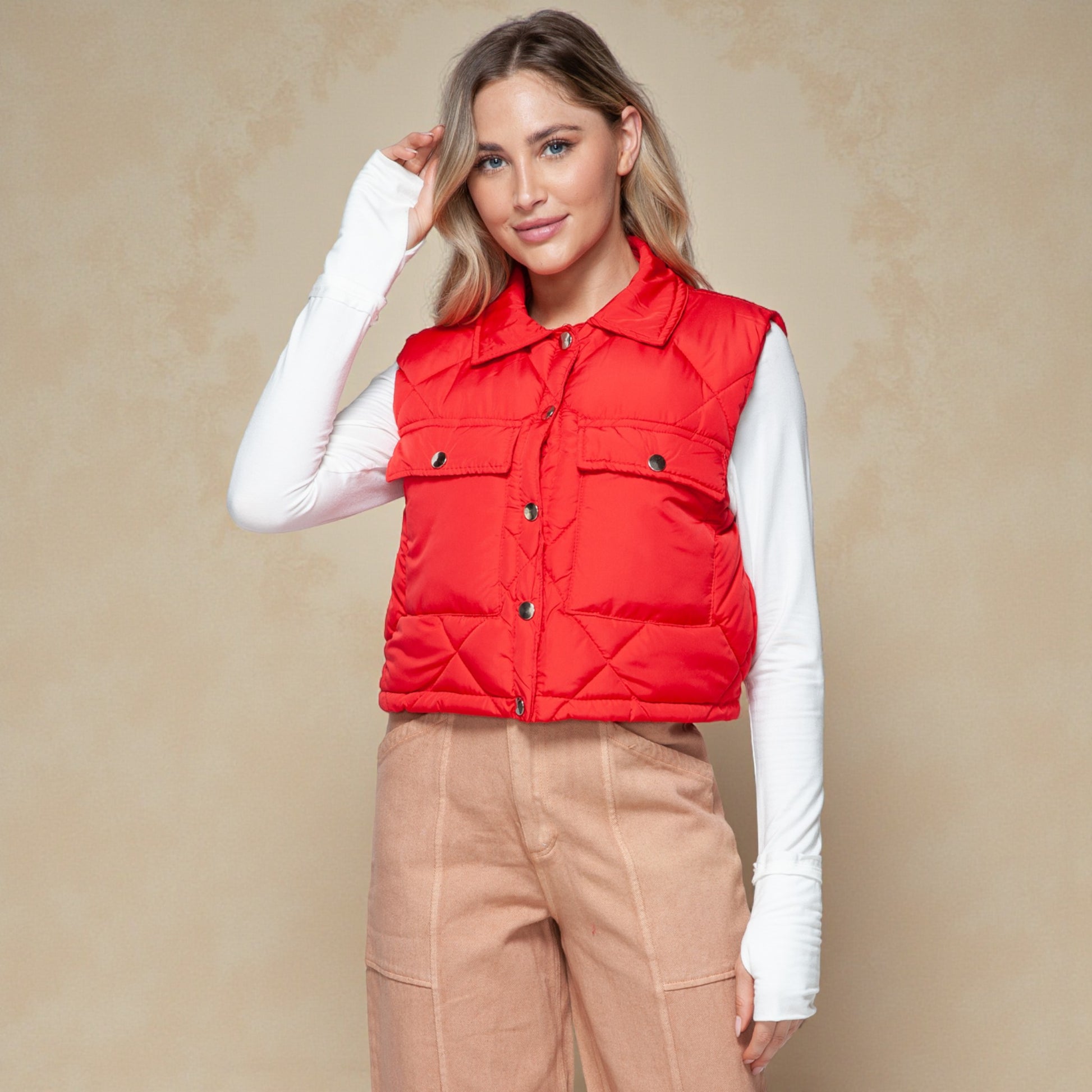 Woman wearing a red puffer vest over a white long-sleeve shirt on a beige background