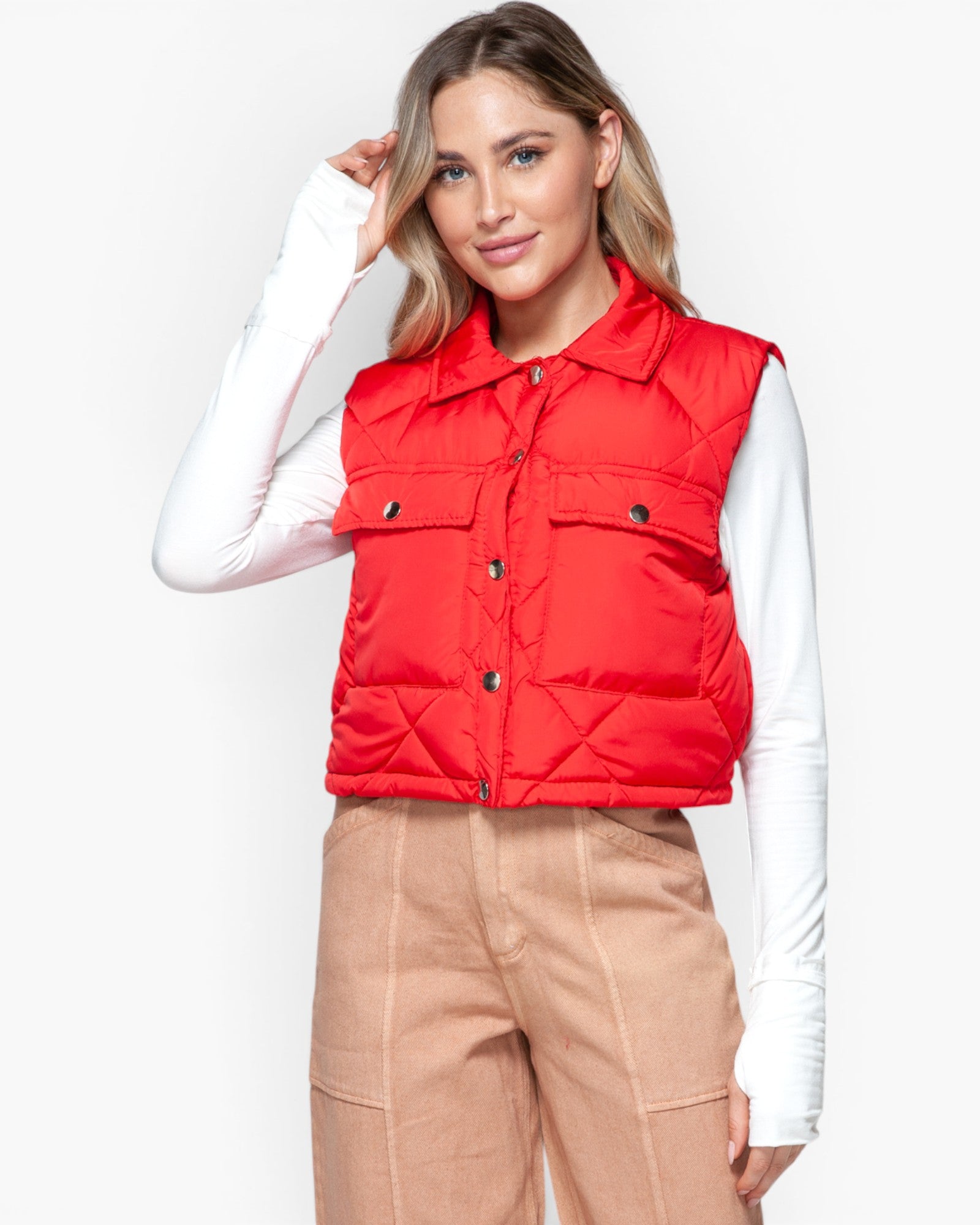 A woman modeling a bright red quilted puffer vest over a white long-sleeve top and beige cargo pants, photographed against a clean white studio background.