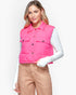 A woman modeling a bright pink sleeveless quilted puffer vest over a white long-sleeve top and tan pants, against a plain light gray studio background.
