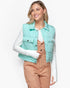 A woman wearing a mint green puffer vest over a white long-sleeve top and tan corduroy overalls, photographed against a clean white studio background.