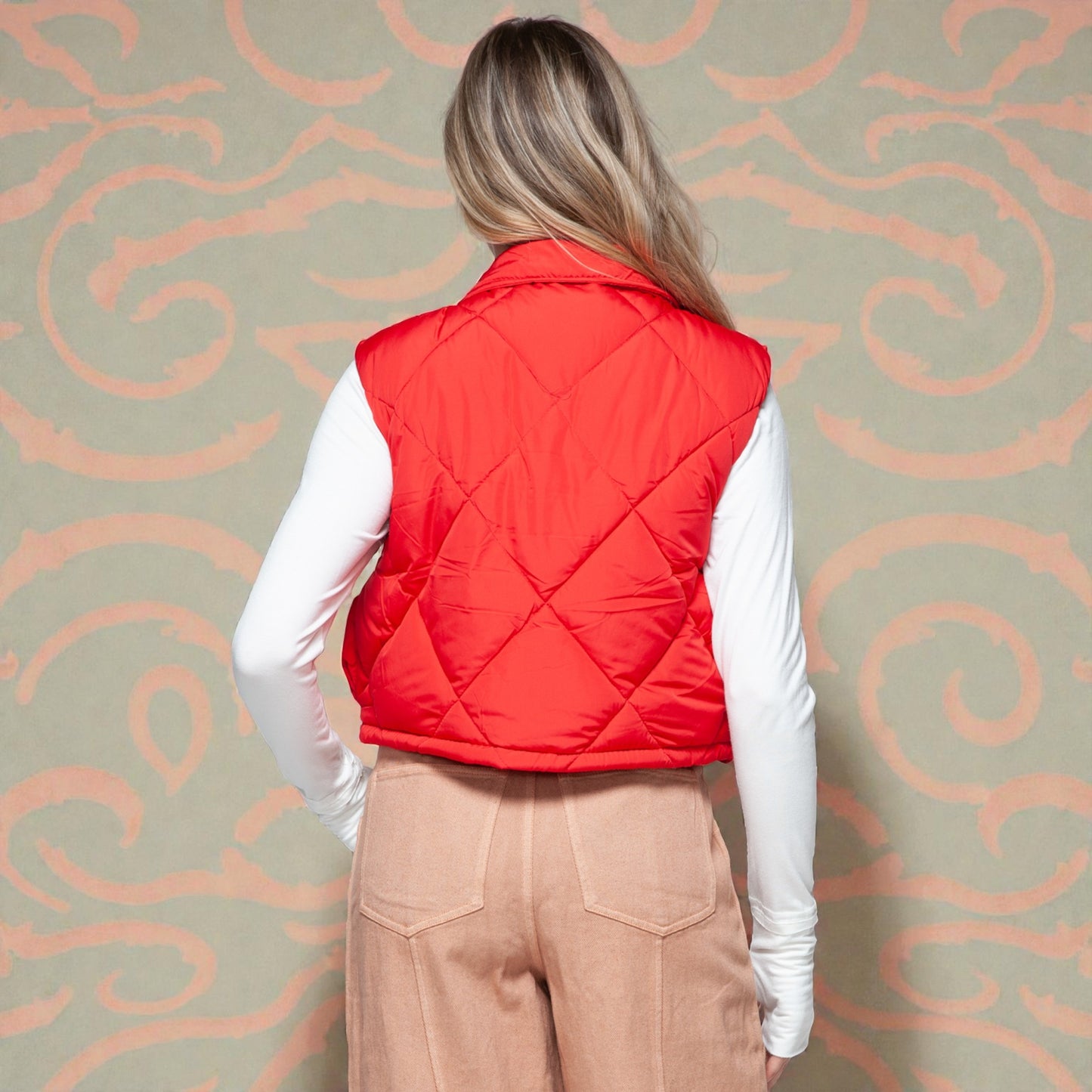 Person wearing a red quilted vest against a patterned wall.