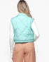 A woman shown from the back wearing a mint green diamond-quilted puffer vest over a white long-sleeve top and peach-colored pants, against a plain white studio background.