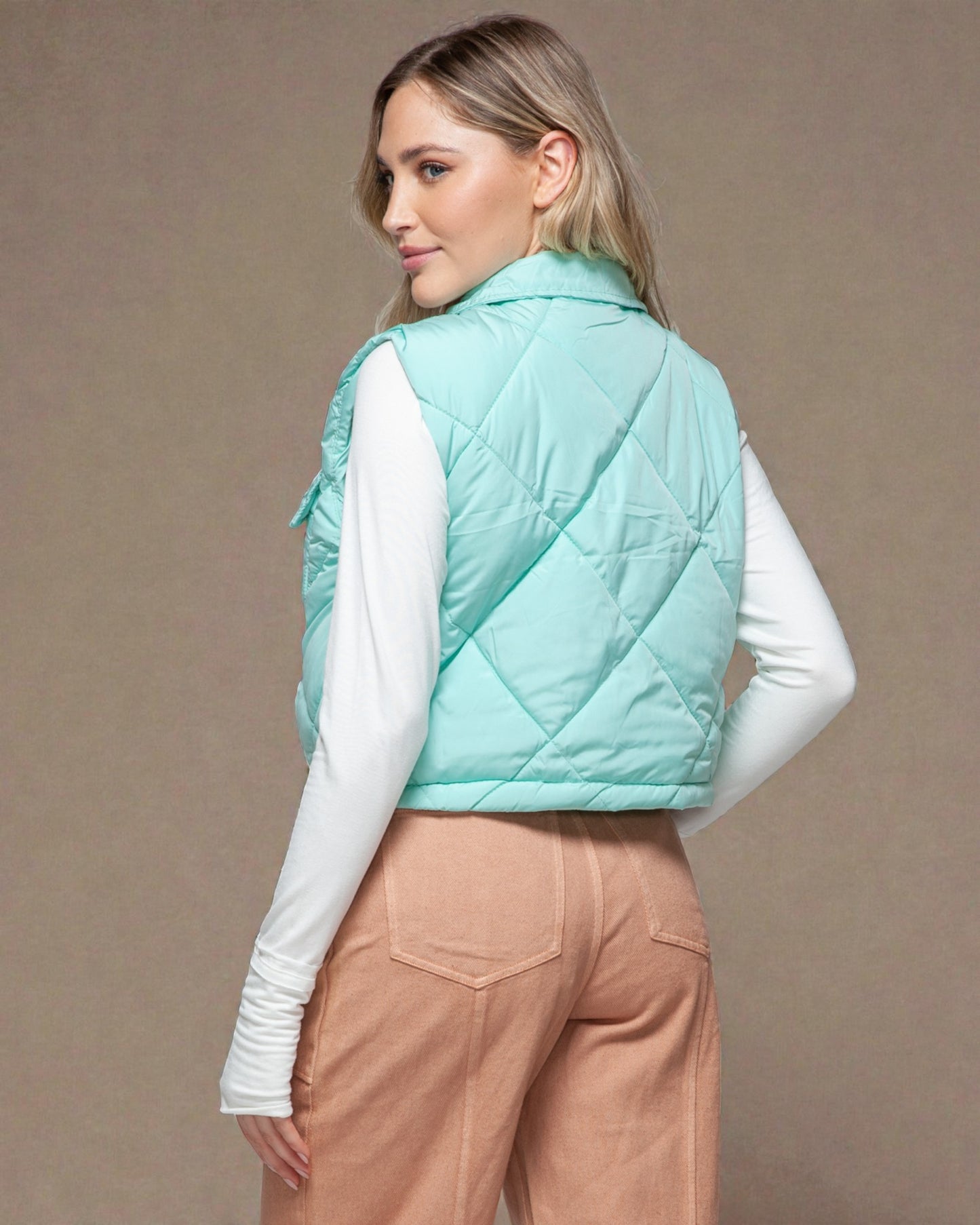 Woman wearing a light blue quilted vest against a beige background