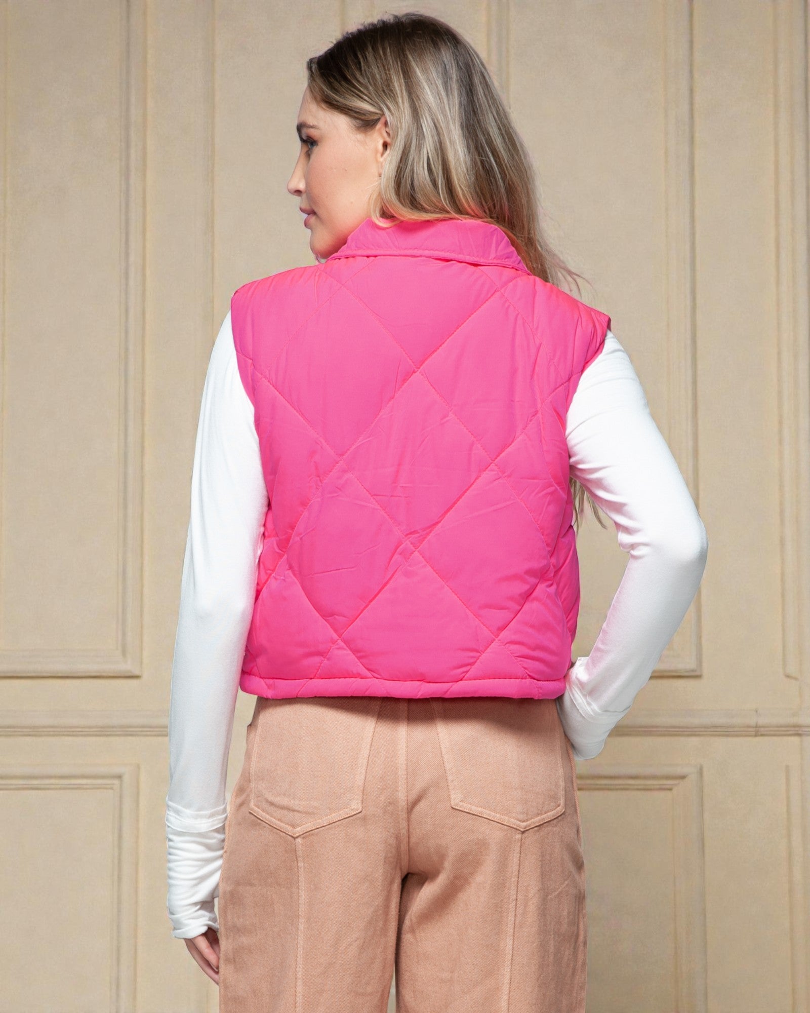 Woman wearing a pink quilted vest against a beige paneled wall