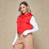 Woman wearing a red puffer vest over a white long-sleeve shirt and beige pants on a patterned background