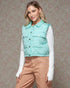 Woman wearing a light blue puffer vest over a white shirt and brown pants on a patterned background
