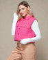 Woman wearing a pink puffer vest over a white shirt with beige pants against a beige background