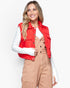 A woman wearing a bright red sleeveless puffer vest over a white long-sleeve top and tan corduroy overalls, photographed against a clean light gray studio background.