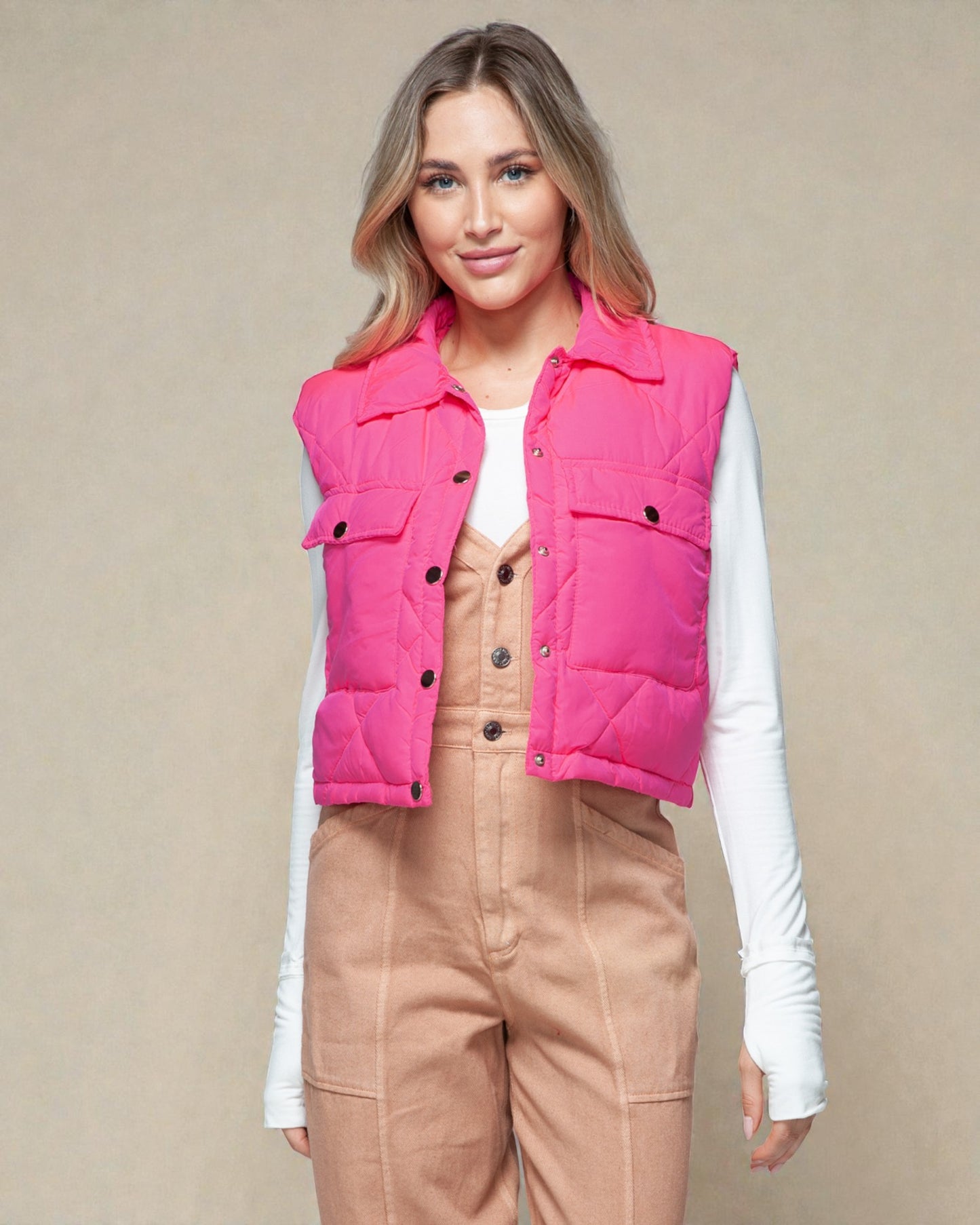 Woman wearing a bright pink puffer vest over a white shirt and beige pants on a beige background