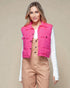 Woman wearing a bright pink puffer vest over a white shirt and beige pants on a beige background