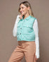 Woman wearing a light blue puffer vest over a white shirt with beige pants on a brown background