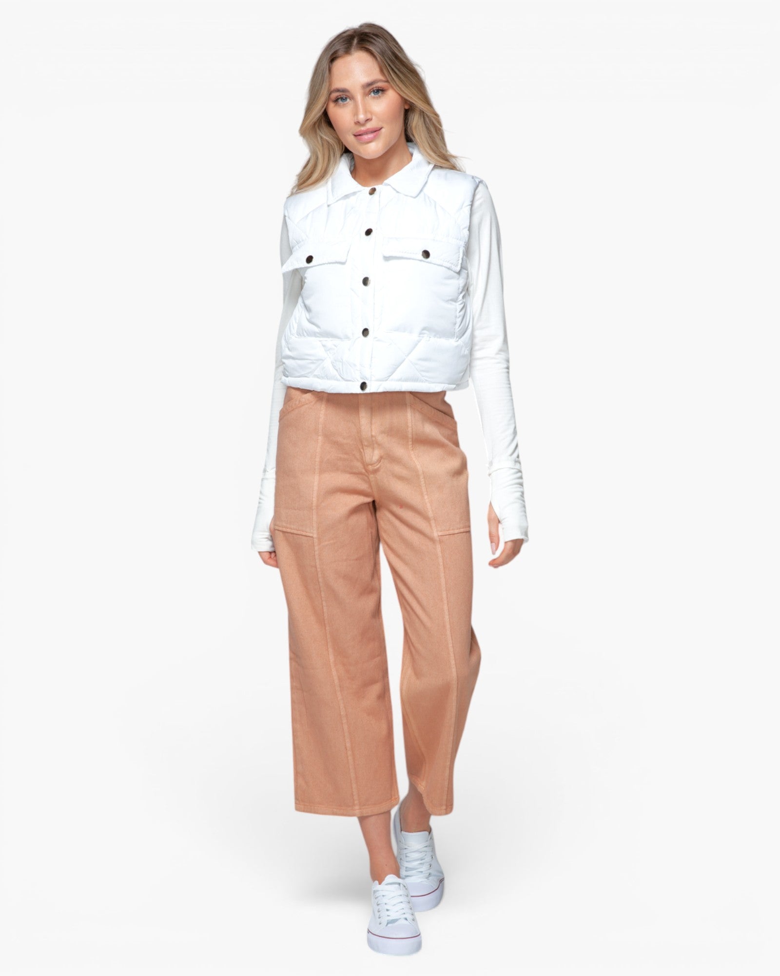 A woman modeling a white quilted button-up jacket over a white long-sleeve shirt, paired with tan cropped wide-leg pants and white sneakers, against a light gray studio background.