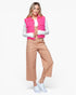 A woman modeling a bright pink sleeveless vest over a white long-sleeve top, paired with tan cropped pants and white sneakers, against a light gray studio background.