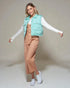 Woman wearing a light blue puffer vest over a white shirt and beige pants on a plain background