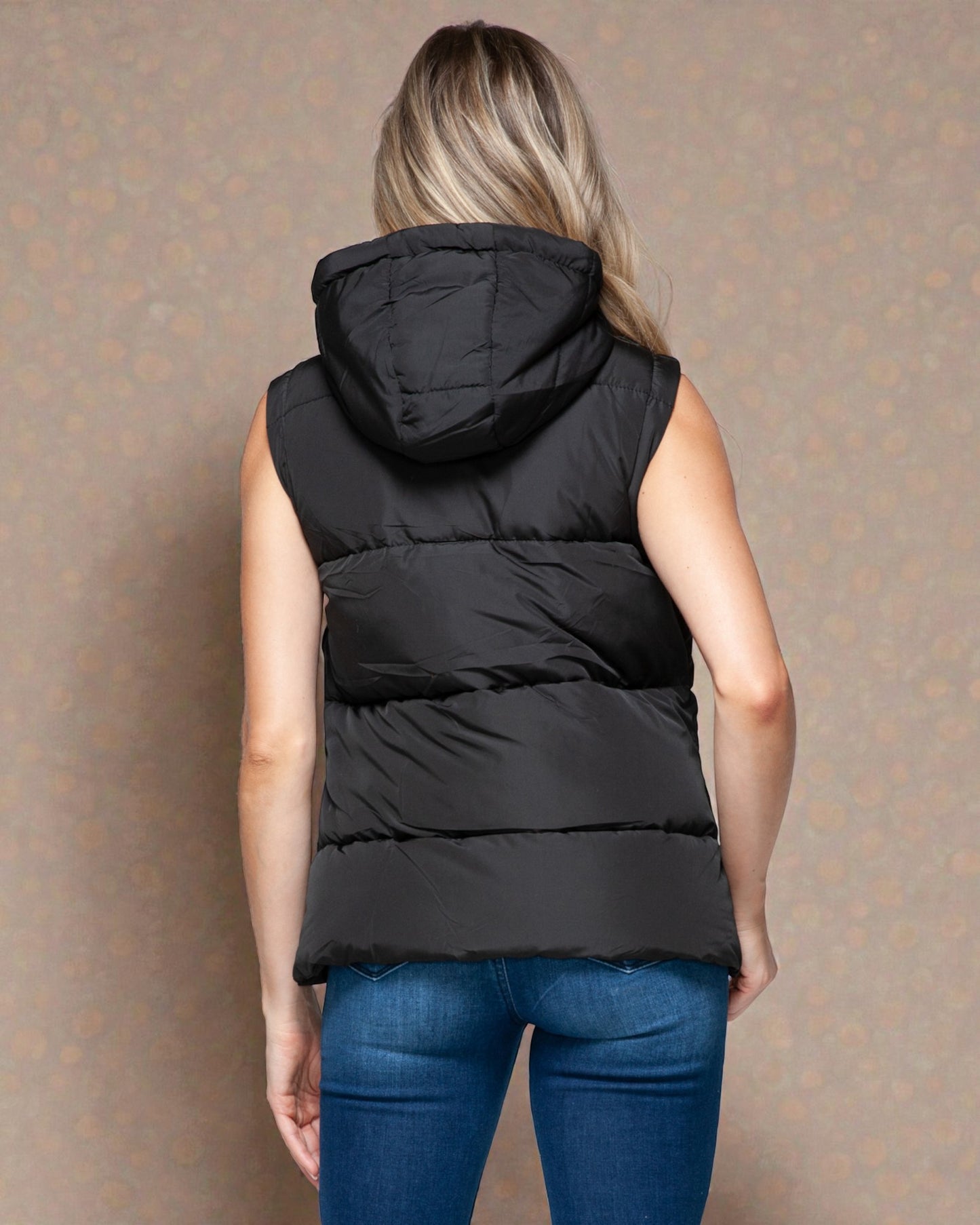 Person wearing a black puffer vest against a patterned wall.