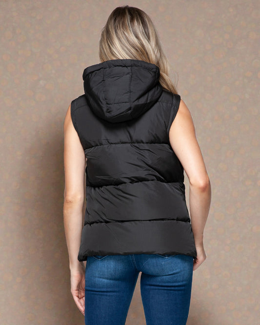 Person wearing a black puffer vest against a patterned wall.