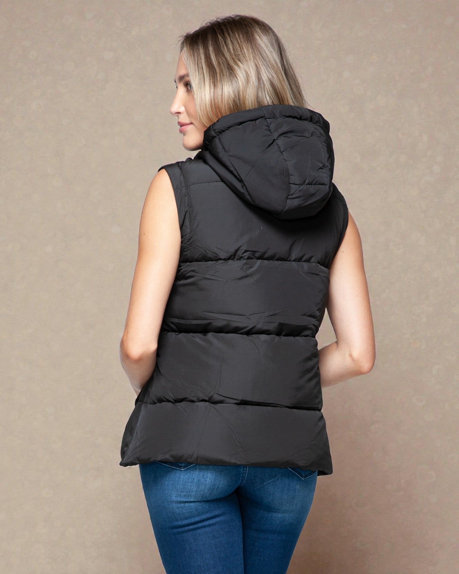 Woman wearing a black puffer vest against a beige background