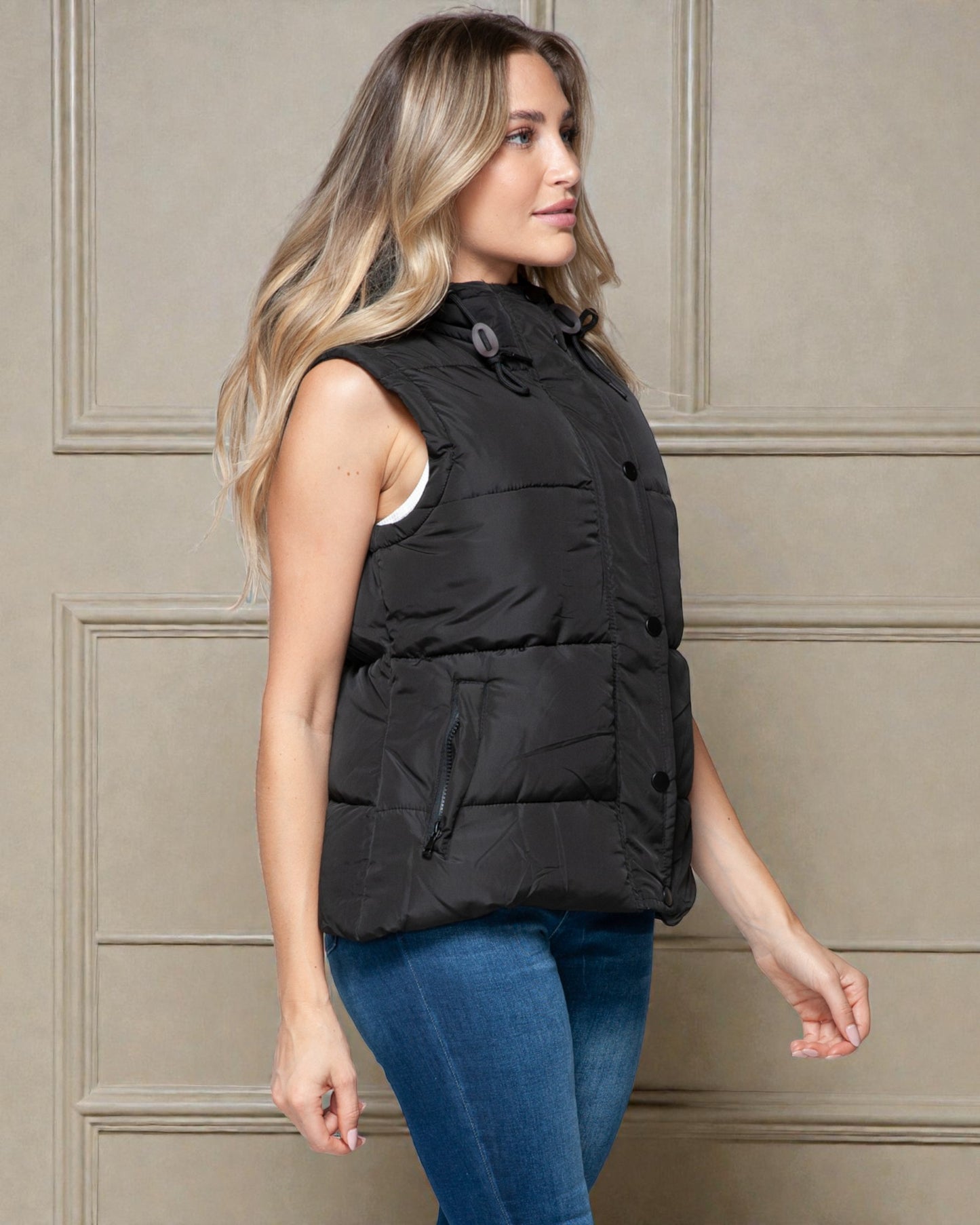Woman wearing a black puffer vest against a beige wall