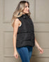 Woman wearing a black puffer vest against a beige wall